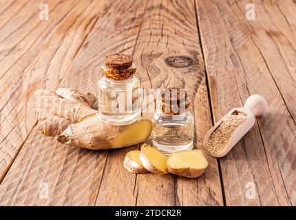 Olio di radice di zenzero naturale fatto in casa in due bottiglie con tappo in sughero su fondo di legno tra le radici di zenzero. Cura di sé a casa Foto Stock