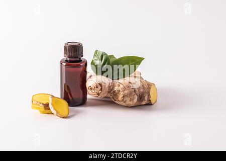 Olio essenziale di radice di zenzero in una bottiglia medica con un tappo su sfondo bianco con fette e radice. Concetto di cura organica Foto Stock
