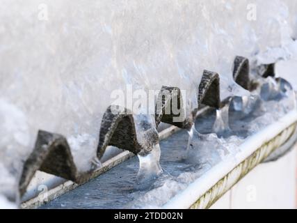 Grondaie congelate. Tetto in amianto coperto di neve e gocciolatoio pieno di ghiaccio. Rimuovere il ghiaccio dalle grondaie Foto Stock