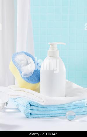 Una bottiglia di gel doccia non etichettata e una spugna sono esposti sugli asciugamani piegati. Scena squisita con due colori principali: Blu e bianco. Mockup cosmetico. Foto Stock