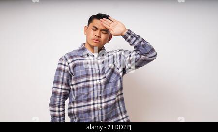 Infelice malato giovane asiatico soffre di un terribile forte dolore alla testa, toccando la fronte con gli occhi chiusi, ripresa in studio, ragazzo adolescente avere febbre durante Foto Stock