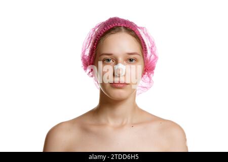 Ritratto di una donna attraente in un berretto rosa con intonaci sul naso dopo la rinoplastica su sfondo bianco dello studio. Foto Stock