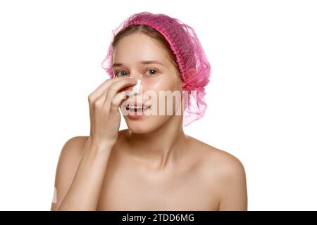 Il ritratto di una donna attraente in un berretto rosa tocca il suo naso con cerotti dopo la rinoplastica su sfondo bianco dello studio. Foto Stock