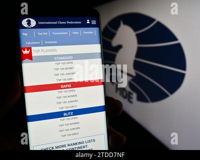 Persona in possesso di cellulare con pagina web dell'organizzazione International Chess Federation (FIDE) davanti al logo. Concentrarsi sul centro del display del telefono. Foto Stock