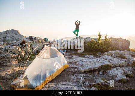 una donna sicura di sé pratica yoga (posa sull'albero) sulla cima della montagna. Foto Stock