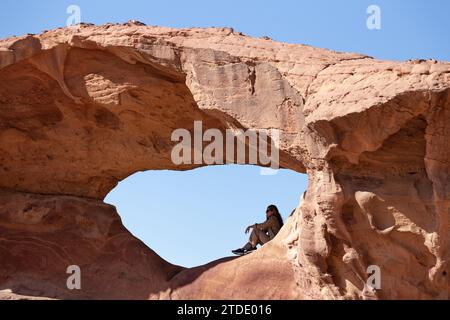 Donna che riposa sotto un arco fatto di roccia rossa, Wadi Rum Foto Stock