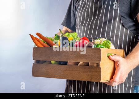 Concetto di shopping del mercato biologico agricolo, scatola di legno con estate, verdure crude e frutta autunnali, mani contadine su sfondo bianco Foto Stock