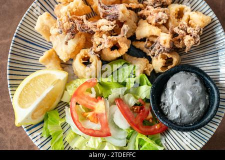 Un'immagine ravvicinata su un piatto di anelli di calamaro calamaro appena fritti, servito con una salsa all'aglio con inchiostro di calamari. Foto Stock