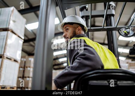 Operaio di magazzini multirazziali che guida un carrello elevatore a forche. Addetto al magazzino che prepara i prodotti per il mennt, consegna, controllo delle scorte in magazzino. Foto Stock