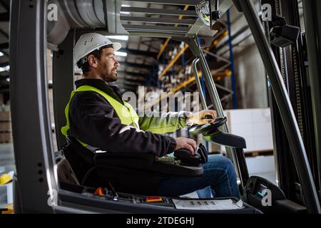 Operaio di magazzini multirazziali che guida un carrello elevatore a forche. Addetto al magazzino che prepara i prodotti per il mennt, consegna, controllo delle scorte in magazzino. Foto Stock