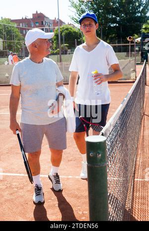 Nonno e nipote che parlano sul campo a giocare a tennis Foto Stock