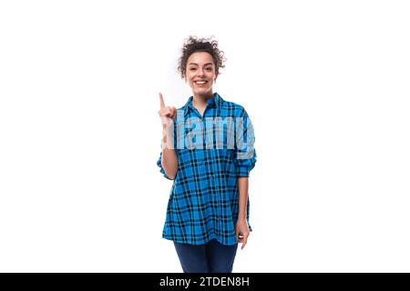 la giovane donna europea dai capelli scuri vestita informalmente con una camicia a quadri blu è ispirata e punta il dito verso l'alto Foto Stock