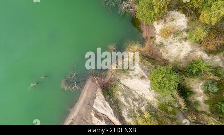 Questa immagine cattura una prospettiva aerea di un'ansa del fiume con acque verde smeraldo adiacenti a una riva boscosa. La riva mostra strati geologici, forse sabbia o argilla, ed è parzialmente erosa, con alberi ai margini che sono indicativi di un clima temperato. Non ci sono animali visibili o attività umane, il che suggerisce una zona naturale, possibilmente isolata. La composizione della foto bilancia l'acqua vibrante con i toni della terra della riva, offrendo un contrasto tra gli ecosistemi acquatici e terrestri. Vista aerea di un'ansa del fiume e di una sponda boscosa. Foto di alta qualità Foto Stock