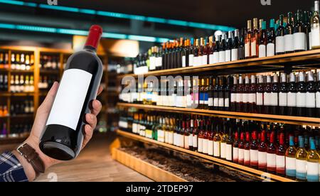 Bottiglia di vino in mano al cliente di fronte al negozio di vini sfocati. Negozio di liquori. Foto Stock