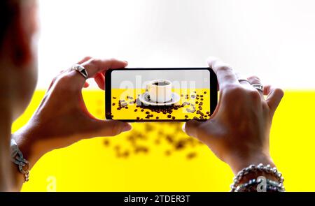 Donna che usa una fotocamera dello smartphone per scattare una foto di un caffè. Durante lo scatto, viene visualizzato sullo schermo della fotocamera mobile. Concetto di fotografia del prodotto. Foto Stock