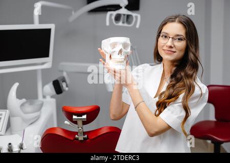 Ritratto del dentista femmina che tiene il modello del cranio e che spiega le regole di igiene dei denti al paziente presso la telecamera. Foto Stock