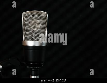 Microfono a condensatore con ampio diaframma dorato su sfondo scuro della superficie insonorizzata della parete dello studio Foto Stock