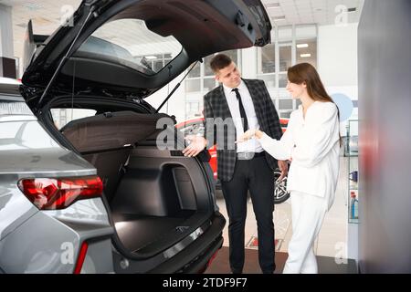 Uomo addetto alle vendite che vende auto presso la concessionaria che presenta un'offerta speciale per le donne Foto Stock