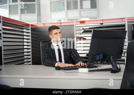 Il concessionario MAN seduto sul posto di lavoro offre contratti di vendita auto nell'ufficio della concessionaria Foto Stock