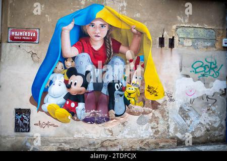 Un murale di una giovane ragazza che si rifugia sotto una bandiera Ucraina a Praga. Street art murale di ChemiS Foto Stock