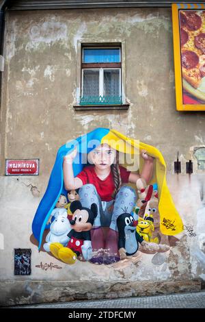 Un murale di una giovane ragazza che si rifugia sotto una bandiera Ucraina a Praga. Street art murale di ChemiS Foto Stock