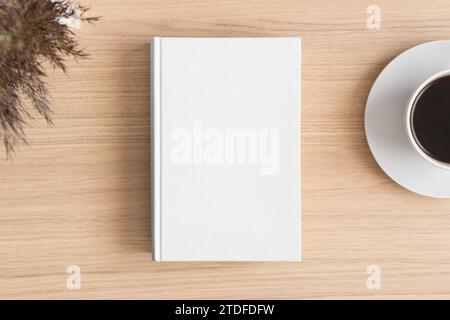 Mockup di un libro bianco con un fiore asciutto e una tazza di caffè sul tavolo di legno. Foto Stock