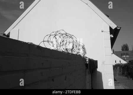 Filo spinato sulla sommità di un muro di mattoni con accanto una casa Foto Stock
