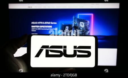 Persona che possiede il cellulare con il logo della società taiwanese ASUSTeK computer Inc (ASUS) davanti alla pagina Web aziendale. Concentrarsi sul display del telefono. Foto Stock
