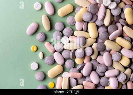 Pillole e compresse di colore pastello su sfondo verde Foto Stock