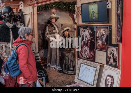 Sarlat-la-Canéda, Nouvelle-Aquitaine, Francia - 23 dicembre 2023: Una bancarella che vende foto di persone vestite in abiti vittoriani al segno di Natale Foto Stock