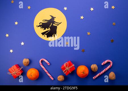 Tradizione del giorno dell'Epifania. La strega Befana vola su scopa su sfondo blu scuro. Caramelle, noci, regali Foto Stock