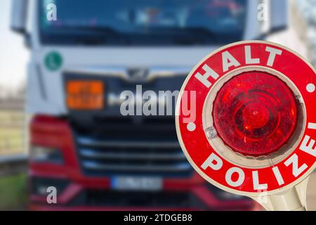 Controllo di polizia (Germania): Primo piano di una cazzuola della polizia con l'iscrizione tedesca HALT POLIZEI (Stop Police) davanti a un camion (composizione) Foto Stock