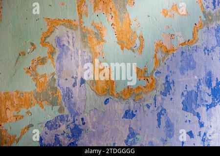 Astratto, dettagliato, colorato motivo testurizzato con strati di vernice blu, verde e arancione peeling multicolore su una vecchia parete esterna in pietra di un edificio Foto Stock