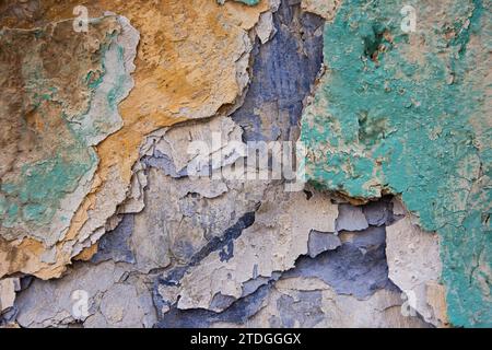 Astratto, dettagliato, colorato motivo testurizzato con strati di vernice blu, verde e arancione peeling multicolore su una vecchia parete esterna in pietra di un edificio Foto Stock