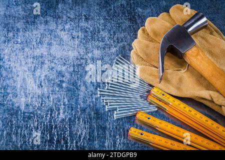 Copia immagine dello spazio di guanti da lavoro in pelle chiodi misuratore di misurazione in legno e martello a griffe su sfondo metallico graffiato concetto di costruzione Foto Stock