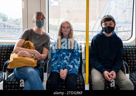 Una madre e due bambini viaggiano su un treno della metropolitana di Londra con maschere facciali per proteggersi da Covid-19 Foto Stock