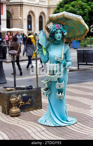 Artista di strada, mimo, statua vivente di una signora Dali, figura fantasy con ombrellone e fiori come parrucca, trucco blu, passanti, la Rambla, Ramblas Foto Stock