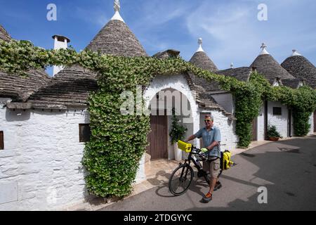 Ciclista tra trulli ad Alberobello, Valle d'Itria, Puglia, Italia Foto Stock