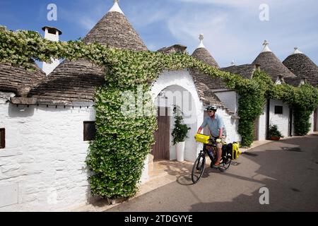 Ciclista tra trulli ad Alberobello, Valle d'Itria, Puglia, Italia Foto Stock