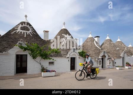 Ciclista tra trulli ad Alberobello, Valle d'Itria, Puglia, Italia Foto Stock