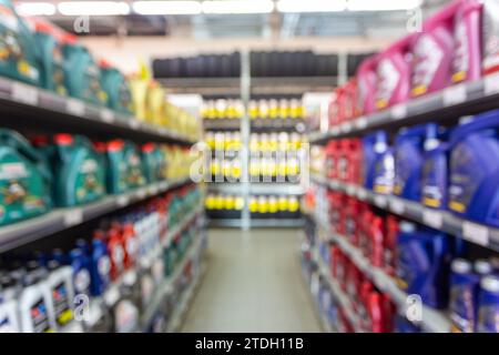 Bottiglie di olio motore colorate sfocate sui ripiani in un punto vendita specializzato. Scaffali con oli motore di vari produttori. Foto Stock