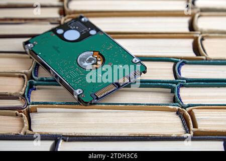 Disco rigido su una pila di vecchi libri di carta squallida. Confronto dei volumi dei supporti di memorizzazione di epoche diverse Foto Stock