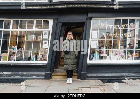 Una donna si trova all'ingresso di un'antica casa tradizionale storta e di un negozio a Canterbury, nel Kent, in Inghilterra. Foto Stock