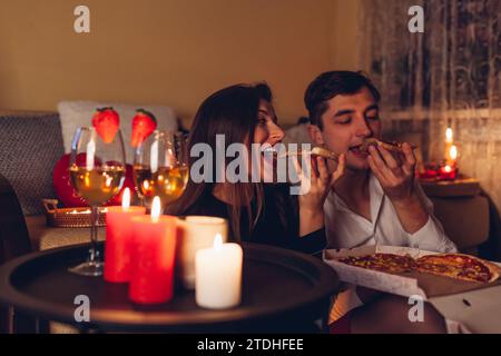 San Valentino coppia in amore mangiare pizza bere vino con fragole avere cena romantica celebrare a casa di notte Foto Stock