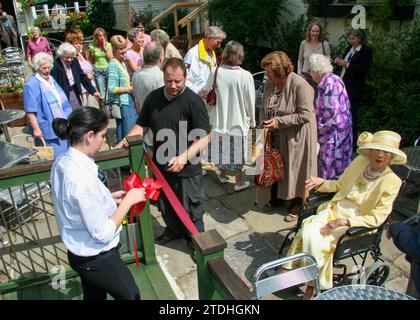 Una signora anziana di giallo limone con un cappello grande apre al nuovo bar/ristorante/sala funzioni sul retro del Crown Hotel Framlingham nel Suffolk Foto Stock