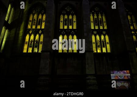 Gruppo centrale della Cattedrale di Bristol di vetrate colorate che raffigurano occupazioni di guerra; illuminato dall'interno di notte. Dicembre 2023 Foto Stock