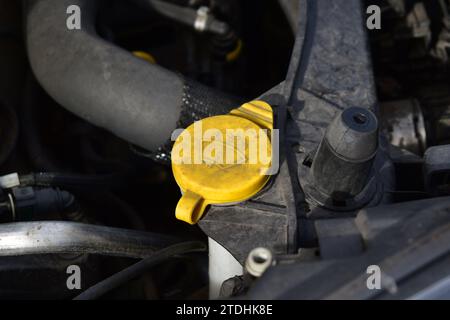 Tappo giallo sporco del serbatoio del liquido tergicristalli all'interno del vano motore Foto Stock