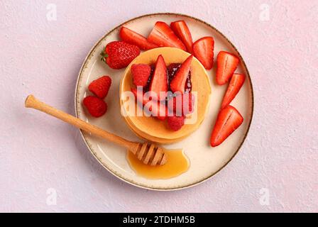 Piatto con frittelle dolci, frutti di bosco e miele su sfondo rosa Foto Stock