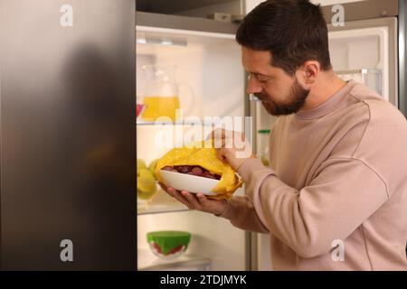 Uomo che mette la ciotola coperta da un involucro di cera d'api in frigorifero al chiuso Foto Stock