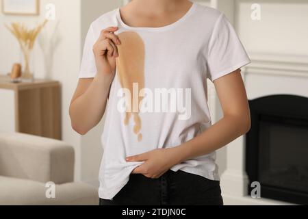 Donna che mostra macchie di caffè sulla camicia al chiuso, primo piano Foto Stock